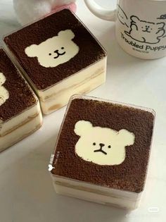 three square brownies with white teddy bears on them next to a coffee mug and stuffed animal