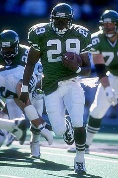 a football player running with the ball in his hand and other players on the field behind him