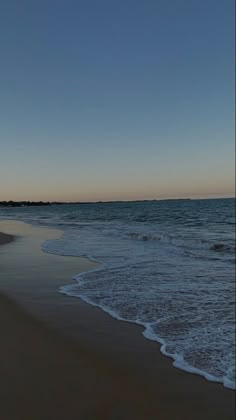 an empty beach with waves coming in to the shore and a blue sky above it