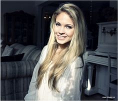 a woman with long blonde hair standing in front of a couch and looking at the camera