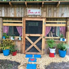 an outdoor chicken coop with several plants in the window and on the ground, next to potted plants