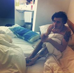 a man sitting on top of a bed covered in white sheets and blankets with tattoos