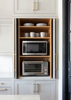 a kitchen with white cupboards and wooden shelves filled with dishes, cups and pans