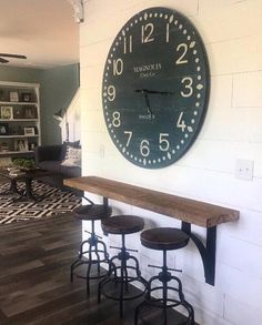 a clock mounted on the wall above bar stools in a room with hardwood floors