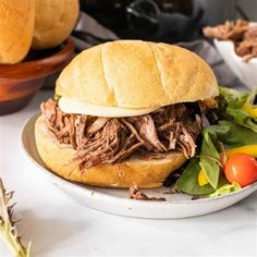 a pulled pork sandwich sitting on top of a plate next to some vegetables and bread