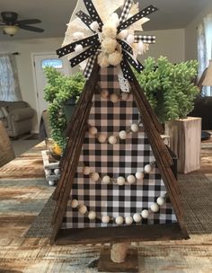 a wooden christmas tree with black and white plaid bow on top, sitting on a table