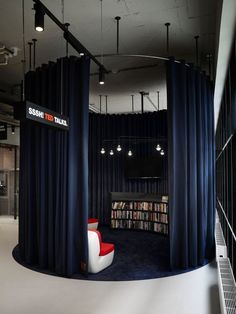 the interior of a library with black curtains and white chairs, bookshelves, and a red chair