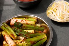 a bowl filled with green vegetables next to another bowl full of noodles and sauces