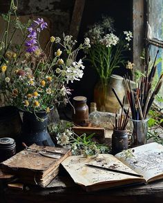 an open book sitting on top of a wooden table next to vases filled with flowers