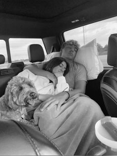 a man and woman sleeping in the back of a car with a dog next to them