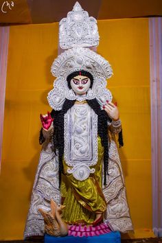 an idol is displayed in front of a yellow wall with white trimmings on it