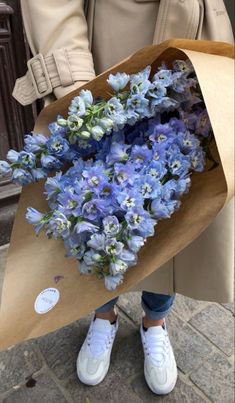 a woman holding a bouquet of blue flowers in her hands and wearing white tennis shoes