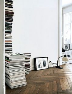 a stack of books sitting on top of a hard wood floor next to a white wall