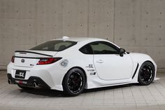 the white sports car is parked in front of a concrete wall with black rims