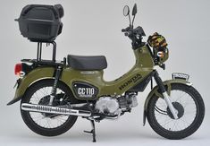 a green motorcycle parked on top of a white floor next to a black seat and back pack