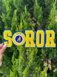 someone holding up the word soror in front of some trees