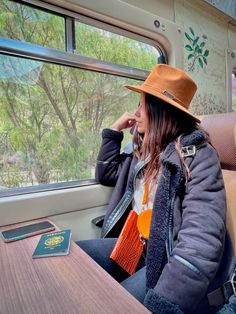 a woman in a hat sitting on a train with her phone to her ear and looking out the window