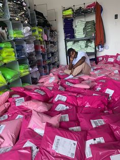 a man sitting on the floor surrounded by pink bags and clothes in a store filled with shirts