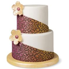 a three tiered cake decorated with flowers and leopard print on the top, sitting on a wooden stand