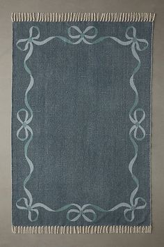 a blue and white rug with fringes on the bottom, in front of a gray wall