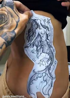 a woman with tattoos on her stomach holding onto a piece of paper that looks like a mermaid