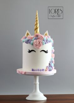 a white cake with pink and blue frosting has a unicorn horn on top