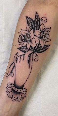 a black and white flower tattoo on the left arm, with an image of a hand holding