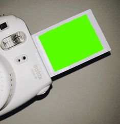 a white camera with a green screen attached to it's back cover on a table