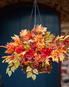 a hanging basket filled with lots of colorful fall leaves and flowers in front of a blue door