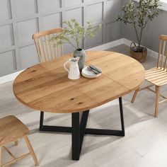 a wooden table with two chairs and a vase on it, in front of a white wall