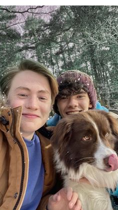 two people and a dog posing for a photo in the snow with trees behind them