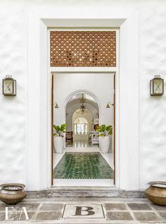 an entrance to a house with potted plants on the floor and two large vases