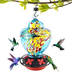 colorful glass bird feeder hanging from a tree branch with two hummingbirds flying around it