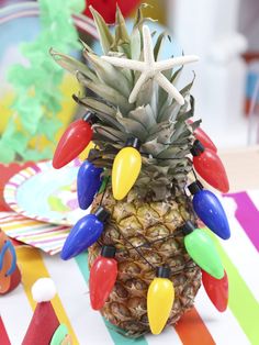 a pineapple decorated with christmas lights on a colorful table cloth at a birthday party