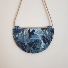 a denim purse hanging from a rope on a white wall with an image of people in the woods