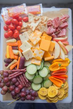 an assortment of cheeses, crackers, and vegetables on a cutting board with grapes