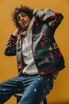 a young man sitting on top of a stool wearing a jacket with letters all over it