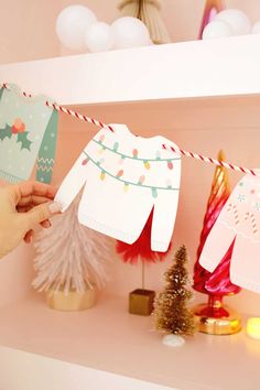 someone holding up some paper clothes on a string next to a christmas tree and other decorations