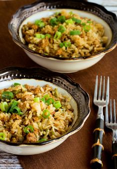 two bowls filled with rice and vegetables next to silverware on a wooden table top