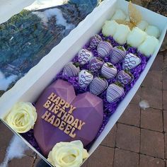 a box filled with lots of purple and white chocolates next to a table topped with flowers