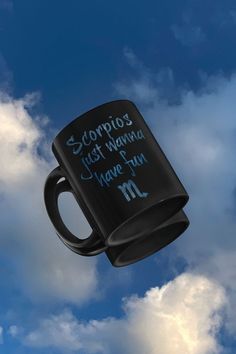 a black coffee mug with writing on it flying in the blue sky above some clouds