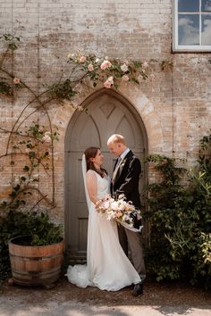 a bride and groom standing in front of an arched doorway with roses on it's side