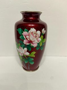 a red vase with pink flowers painted on the side and green leaves in the middle