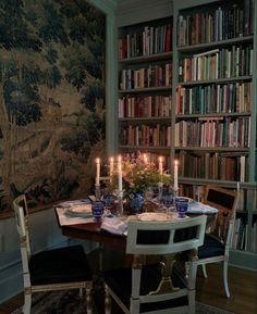 a dining room table is set with plates and candles in front of bookshelves