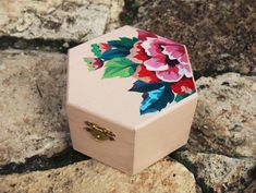 a small wooden box with flowers painted on it sitting on some rocks next to the water