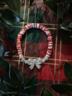 a red and white bracelet with bows on it sitting next to some green leafy plants