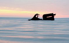 an old boat sitting in the middle of the ocean