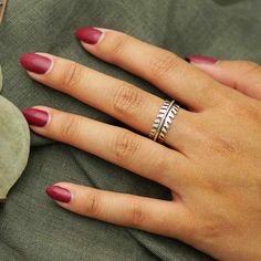 a woman's hand with red nail polish and ring on her left hand, sitting next to a plant