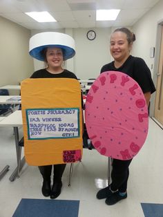 two women standing next to each other holding up signs and paper hats on their heads