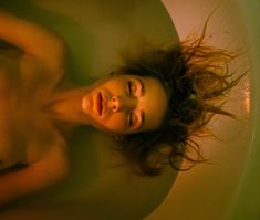 a woman laying in a bathtub with her hair blowing back and eyes closed to the side